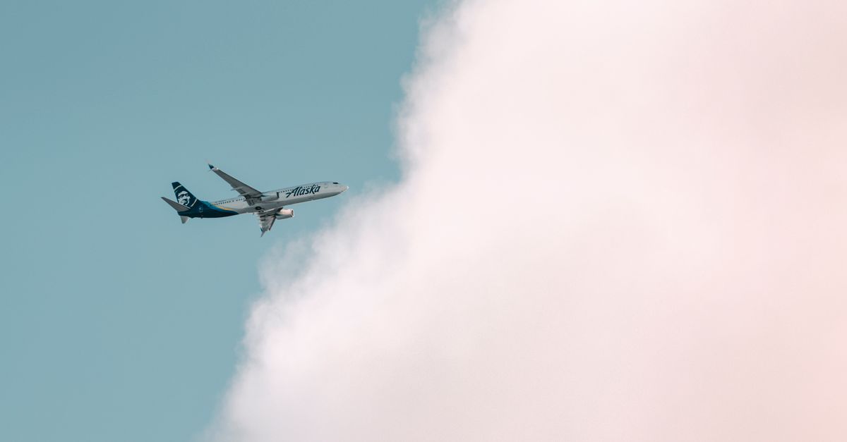 Photo by Cody Alaska Airlines plane soaring through a bright sky with fluffy clouds in Seattle.