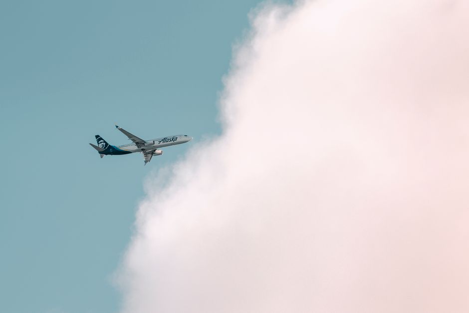 Photo by Cody Alaska Airlines plane soaring through a bright sky with fluffy clouds in Seattle.