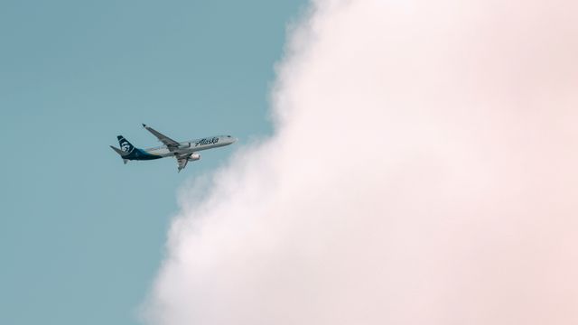 Alaska Airlines plane soaring through a bright sky with fluffy clouds in Seattle. — lounges at Seattle Airport