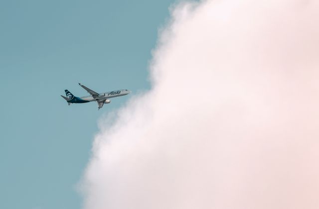 Alaska Airlines plane soaring through a bright sky with fluffy clouds in Seattle. — arriving in Seattle