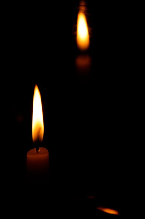 Free A close-up of a single lit candle in a dark environment with reflection. Stock Photo
