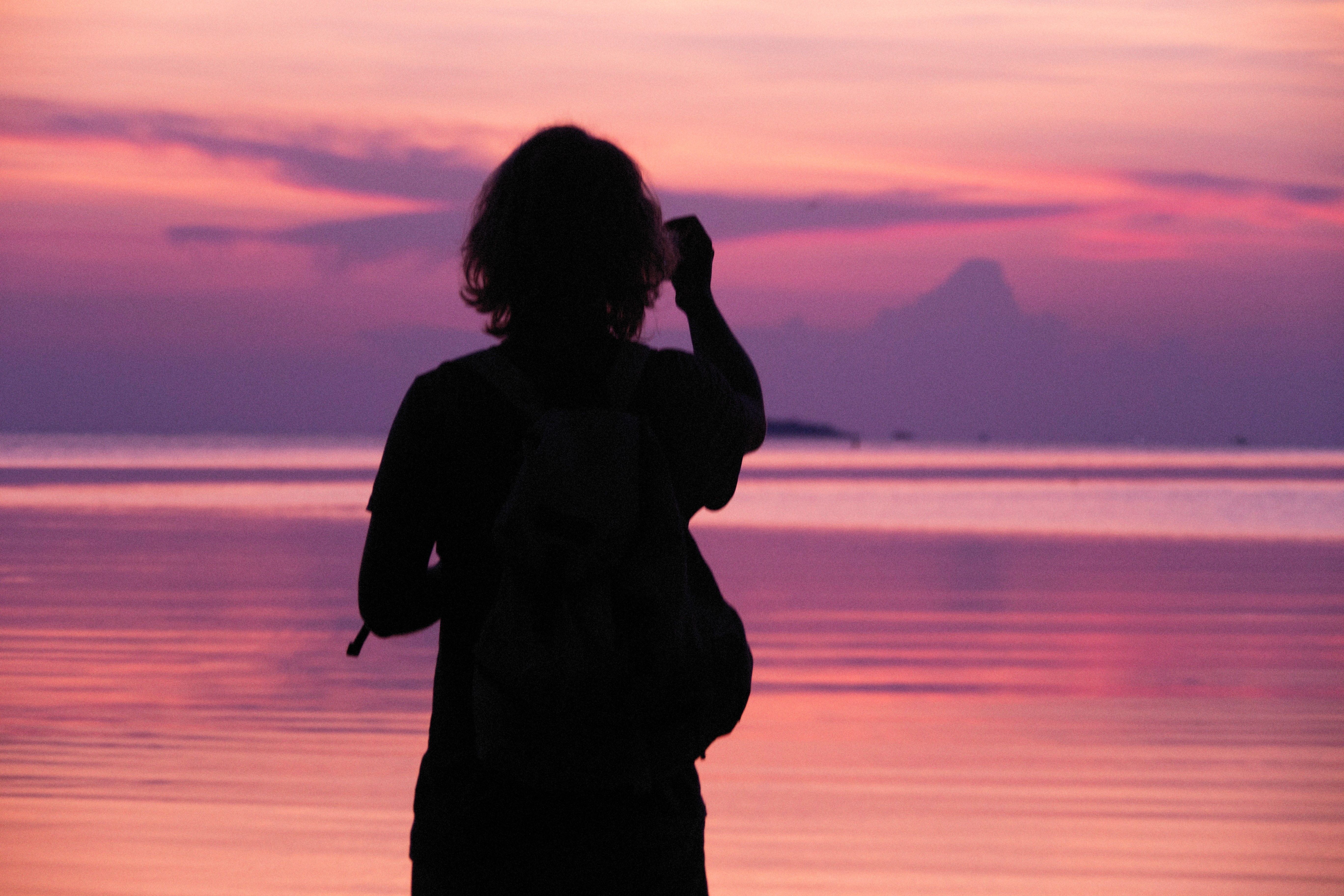 Silhouette of a person with backpack enjoying a serene ocean sunrise.
