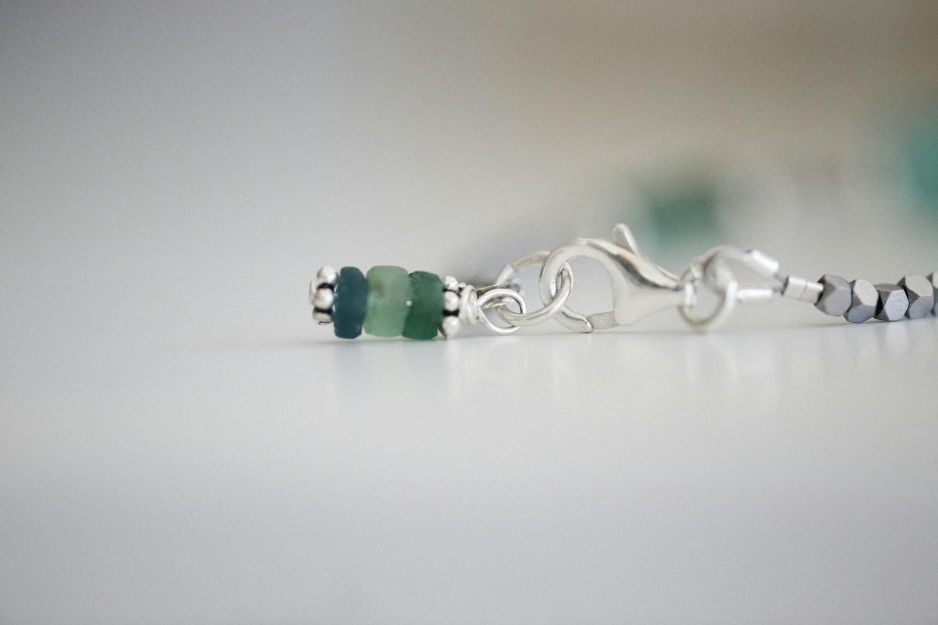 Detailed close-up of silver jewelry with blue and green beads on a white background.