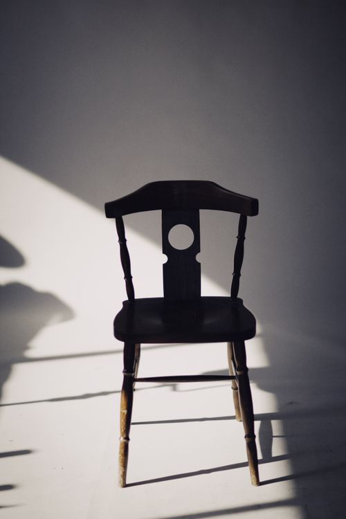 Free A vintage wooden chair casting a shadow in a sunlit room, creating a serene ambiance. Stock Photo