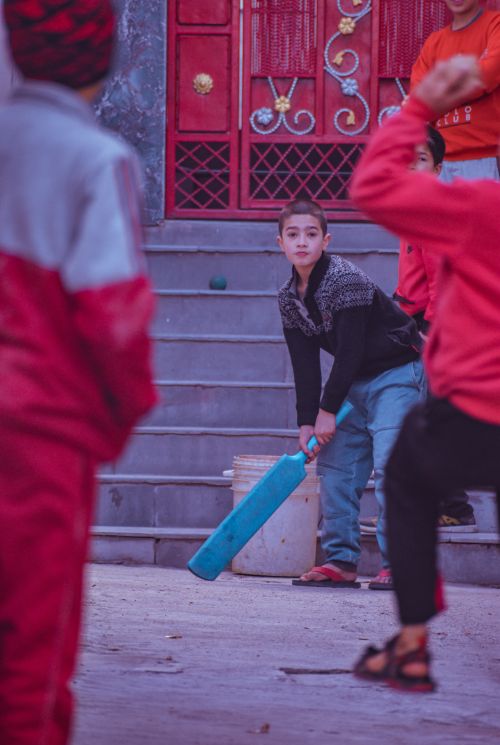 Free Energetic boys playing street cricket on steps, showing concentration and sportmanship. Stock Photo