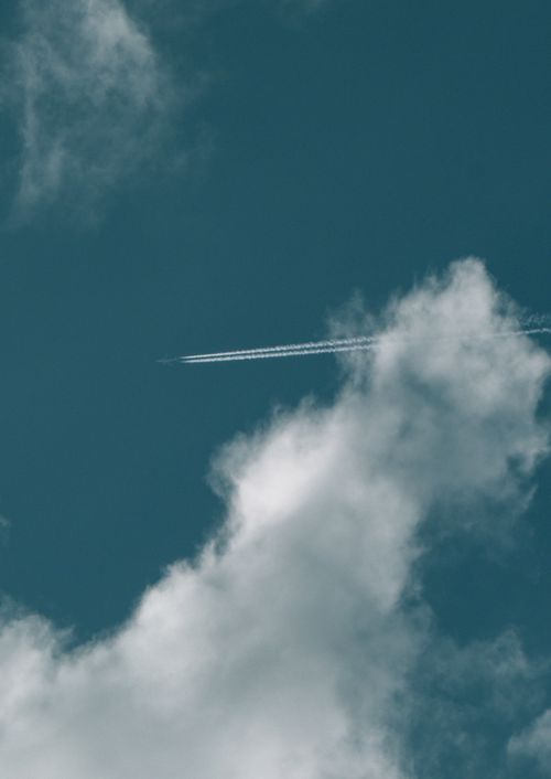Free A plane leaves a trail in a clear blue sky with fluffy white clouds, creating a serene scene. Stock Photo