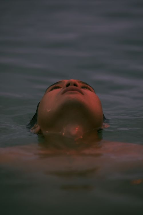 Free A peaceful moment captured as a person enjoys floating in calm water during twilight. Stock Photo