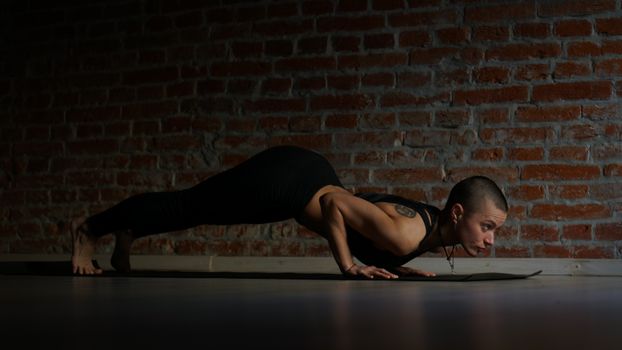 Woman in a low yoga pose on a mat against a brick wall, focused and calm.
