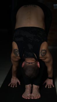 A person in a yoga pose, emphasizing flexibility and tattoos, in soft lighting.
