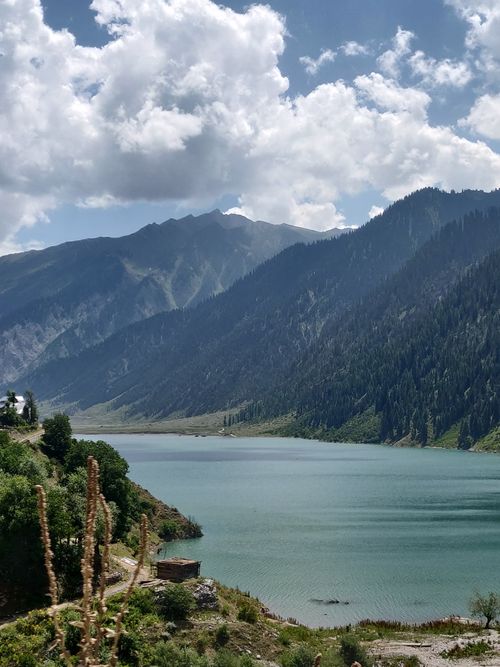 Free Beautiful mountain lake surrounded by lush greenery under dramatic clouds. Stock Photo