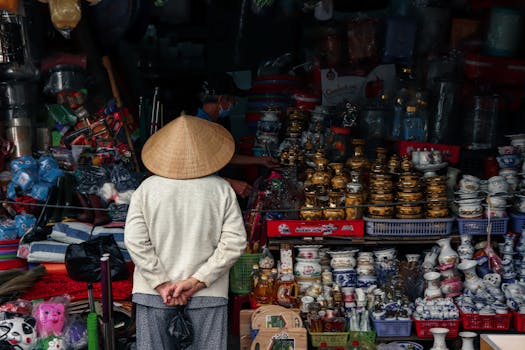 A person in traditional clothing stands at a vibrant market stall offering diverse crafts and goods.