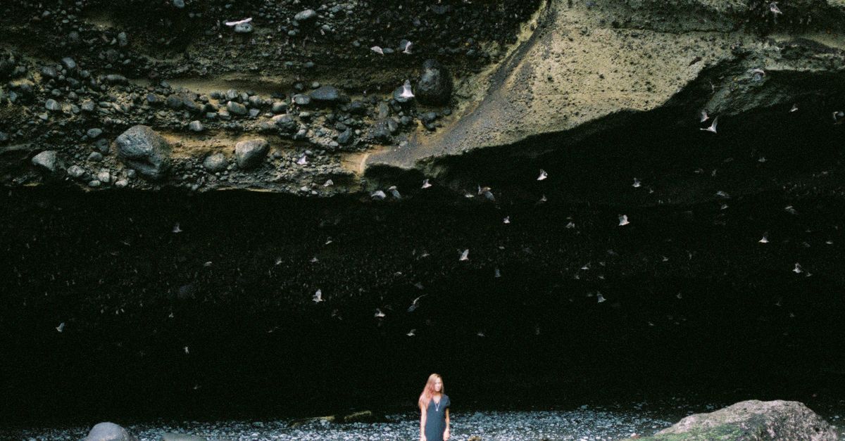 Person Looking Under Rocks Woman Walking near Cave under Rocks on Sea Shore · Free Stock Photo
