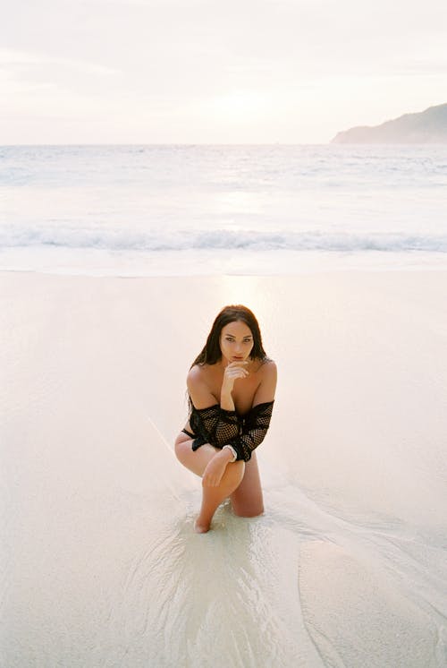 Woman Kneeling in the Sea on the Sandy Beach 