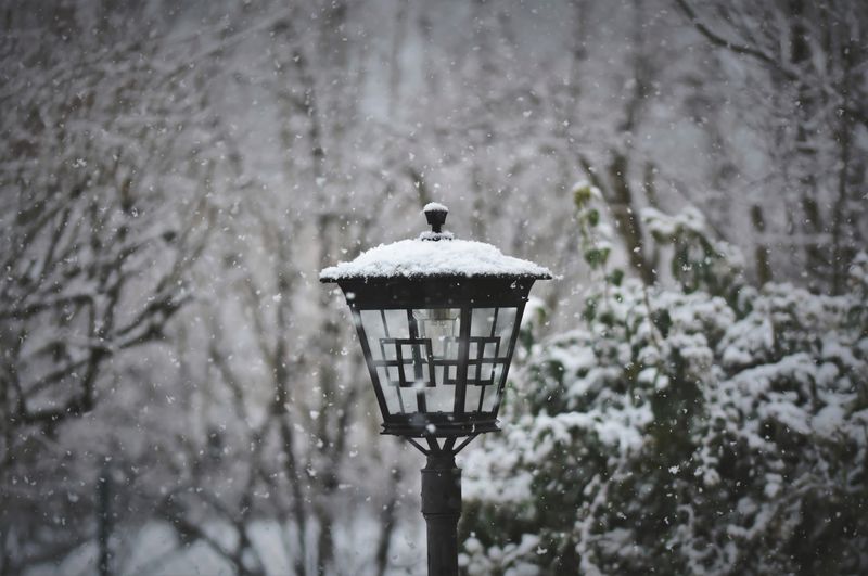 Vintage lamp post covered in snow in a forest during a snowfall, illustrative photo