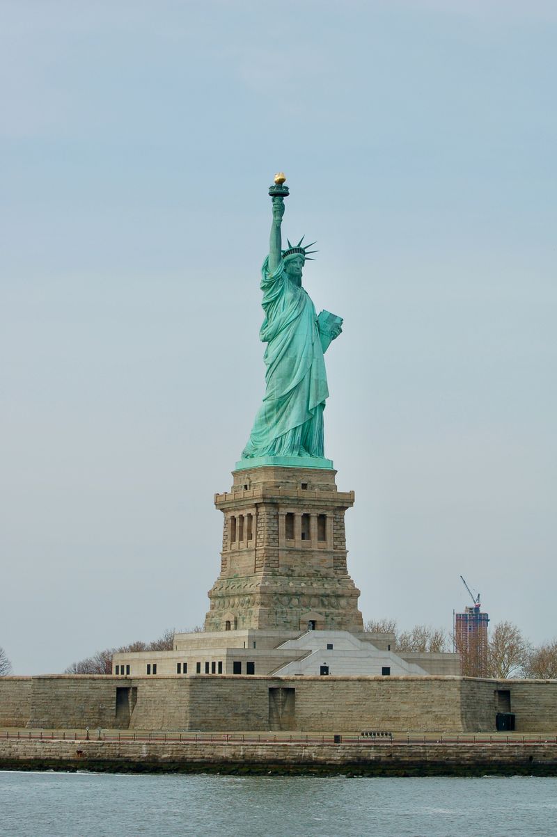 The Statue of Liberty standing on its stone pedestal against a pale sky