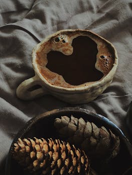 Vintage ceramic coffee cup with natural pinecones on a cozy, soft fabric background.