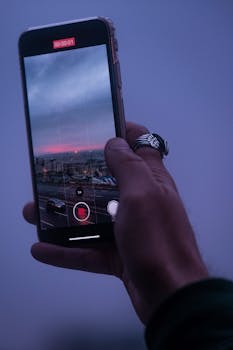 Close-up of a hand holding a smartphone, recording the Istanbul skyline at dusk.
