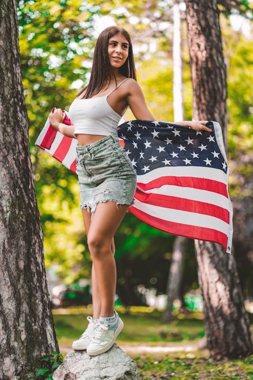 Woman Holding a Flag of America While Standing on a Rock