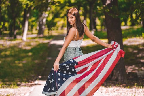 Free Young woman holding American flag outdoors, embracing patriotism with a smile. Stock Photo
