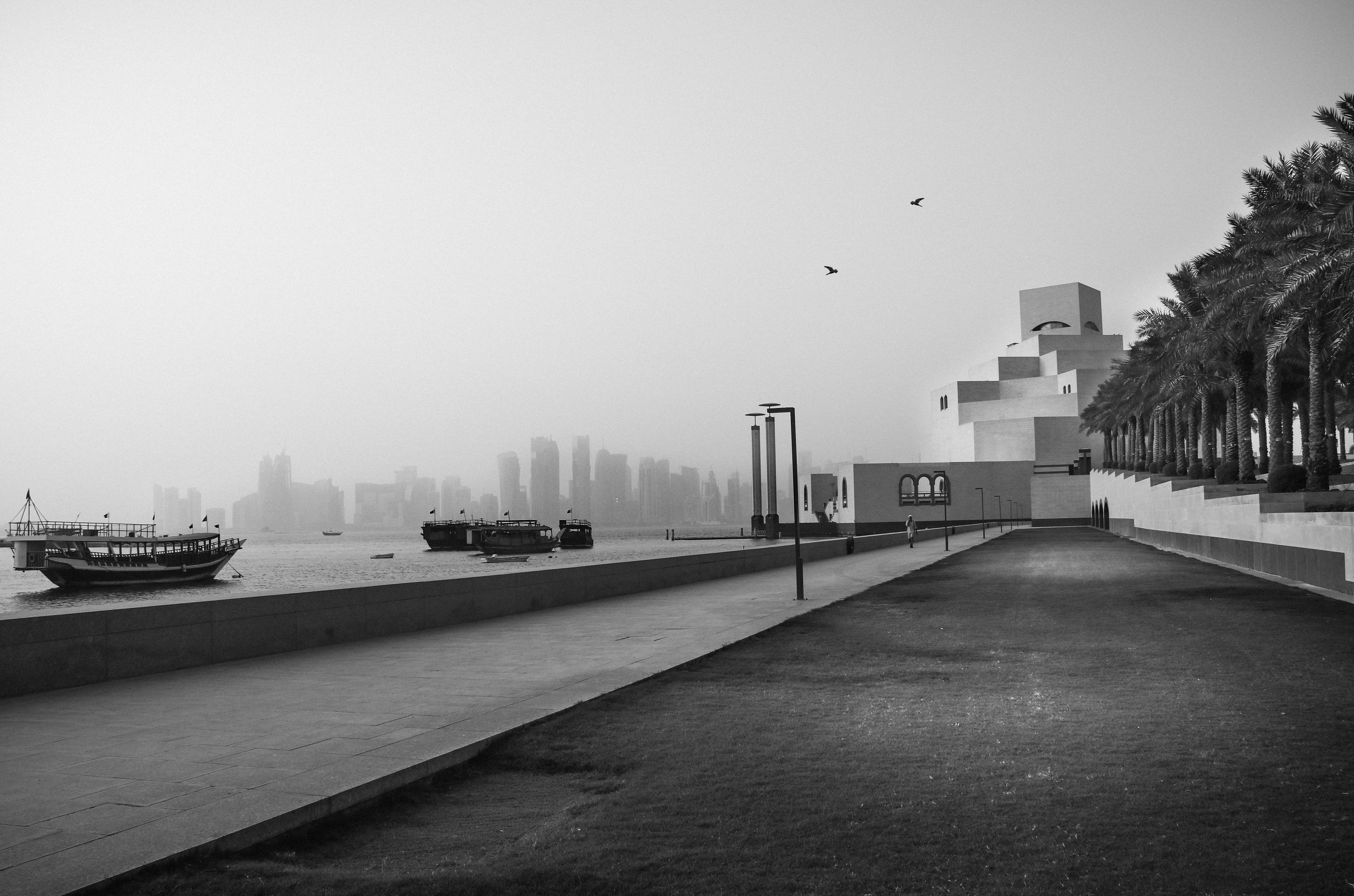 Black and white image capturing the Museum of Islamic Art and Doha skyline with boats in the foreground.