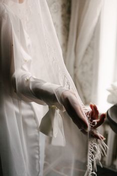 A close-up of a bride's hand holding a delicate wedding veil indoors, emphasizing elegance.