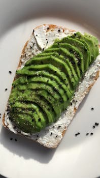 Sliced avocado on cream cheese toast garnished with black sesame seeds, styled on a white plate.