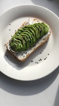 Delicious avocado toast topped with black sesame seeds on a white plate. Perfect for breakfast or lunch.