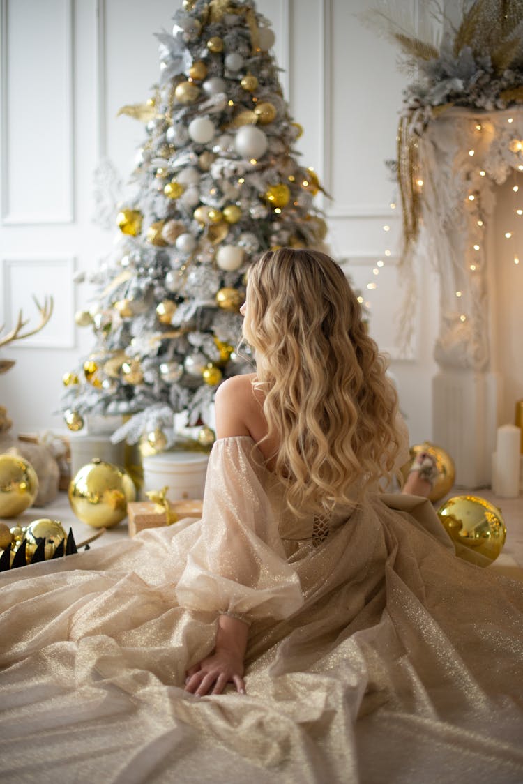 Woman In Dress Sitting Next To Christmas Tree