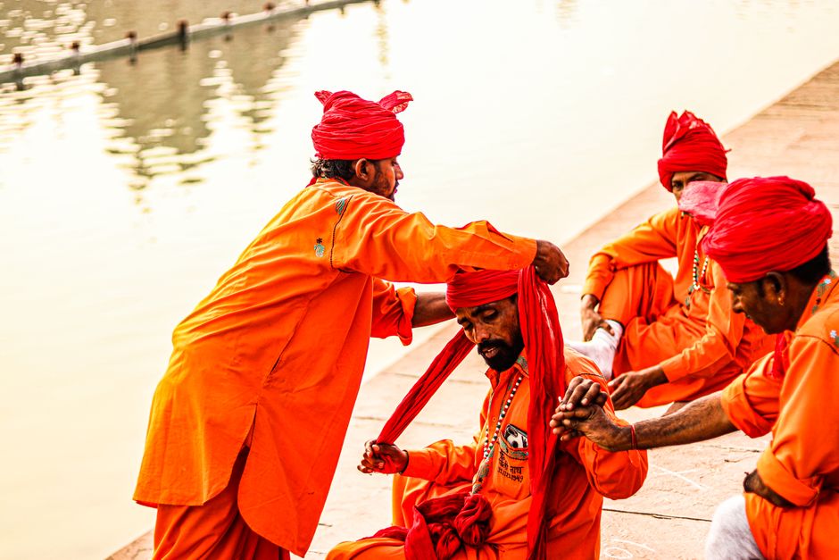 Men in vibrant orange traditional clothing with turbans by a riverside, sharing a cultural moment.