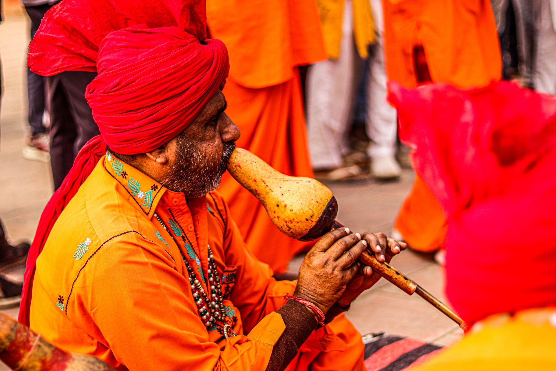 An Indian musician dressed in vibrant attire plays a traditional musical instrument outdoors.