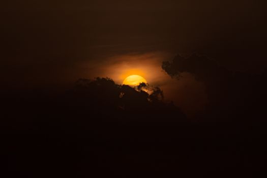 A dramatic sunset with the sun partially hidden behind dark storm clouds, creating a moody atmosphere.