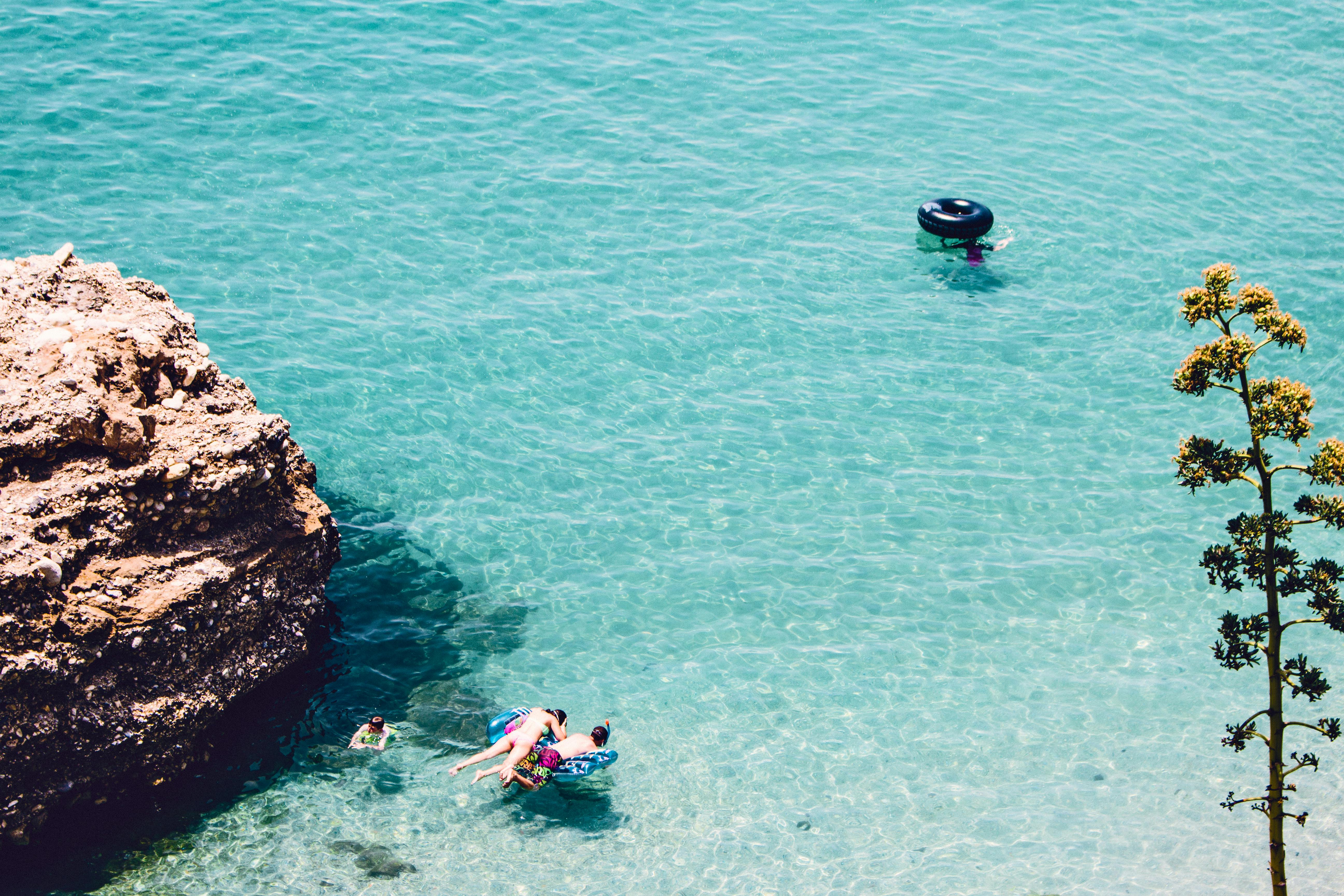 man and woman swimming in the sea near brown cliff