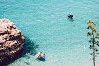 在地中海清澈的蓝色海水里，人们靠近岩石海岸线，游泳、漂浮，享受着阳光明媚的日子