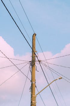 Utility pole with crossing power lines set against a pastel sky, ideal for tech themes.