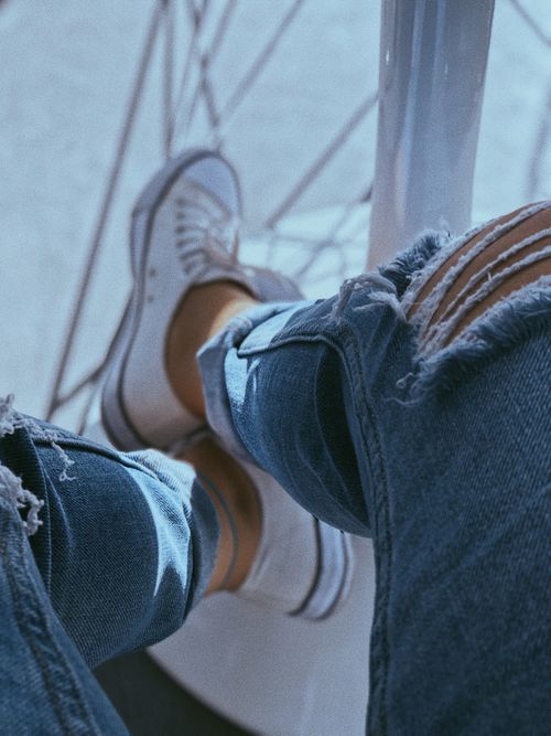 Free Close-up of a casual outfit featuring ripped jeans and white sneakers, perfect for everyday wear. Stock Photo