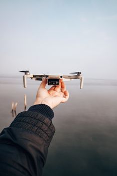Close-up of a person holding a drone by a serene lake on a clear day.