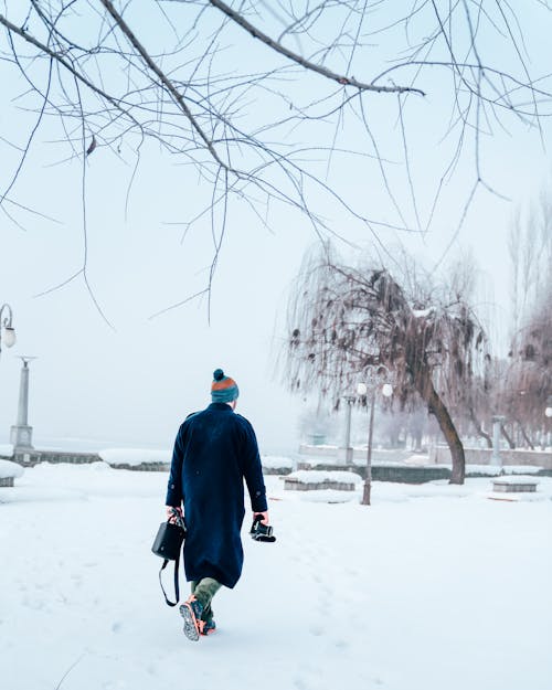 Person in Winter Clothes Walking on Snow Covered Ground