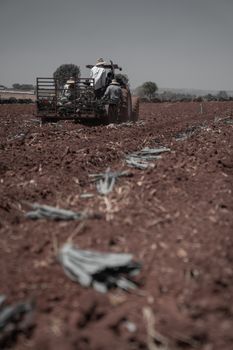 A tractor plowing a field with workers during a clear day in a rural landscape.