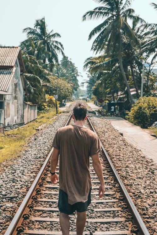 코코넛 야자수 근처 기차 레일에 서있는 갈색 셔츠에 남자