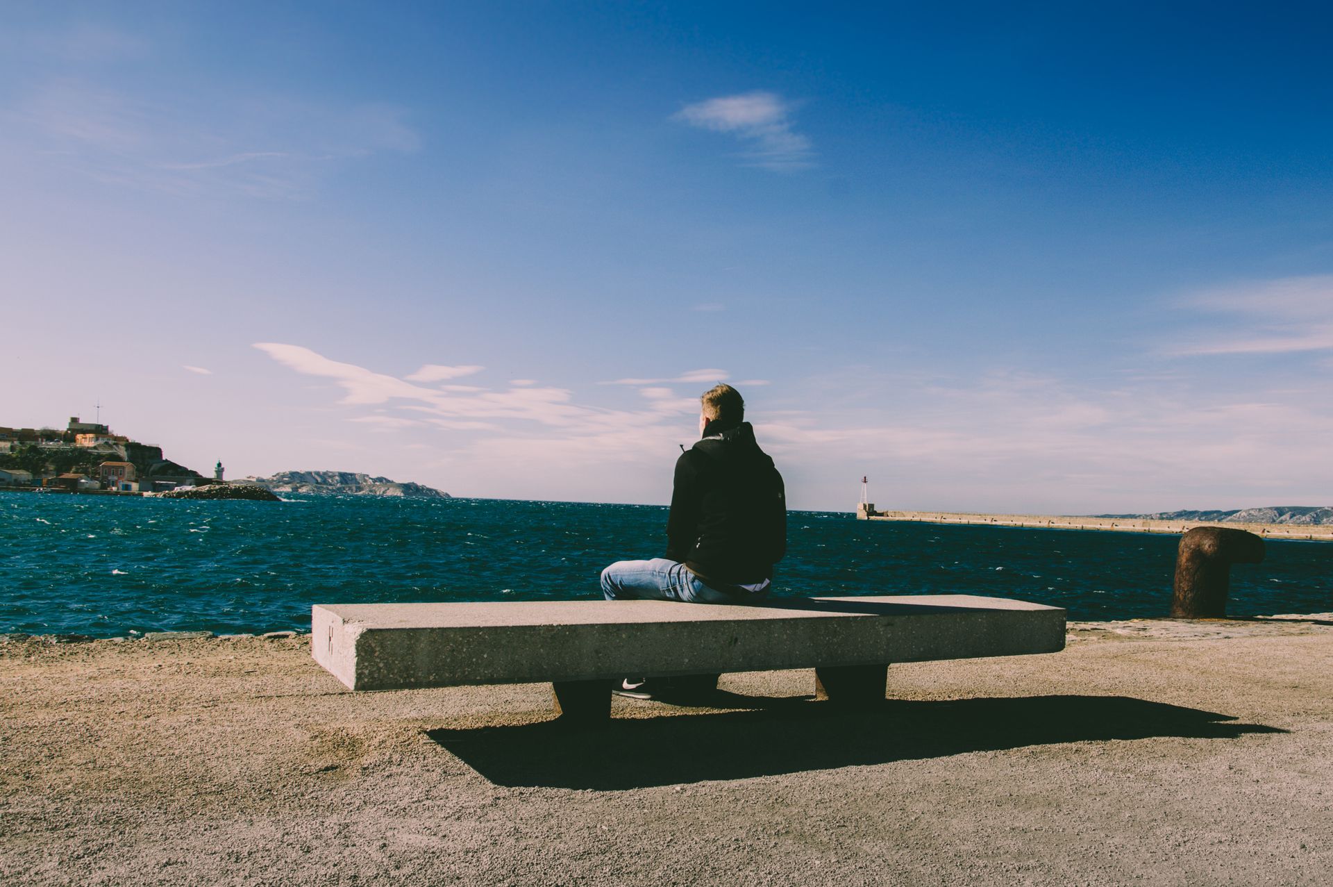 Man sits alone on a bench by the coastline in Marseille. Perfect blend of tranquil sea and sky.