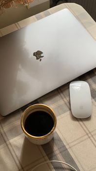 A comfortable setup featuring a laptop, wireless mouse, and a cup of coffee on a plaid tablecloth.