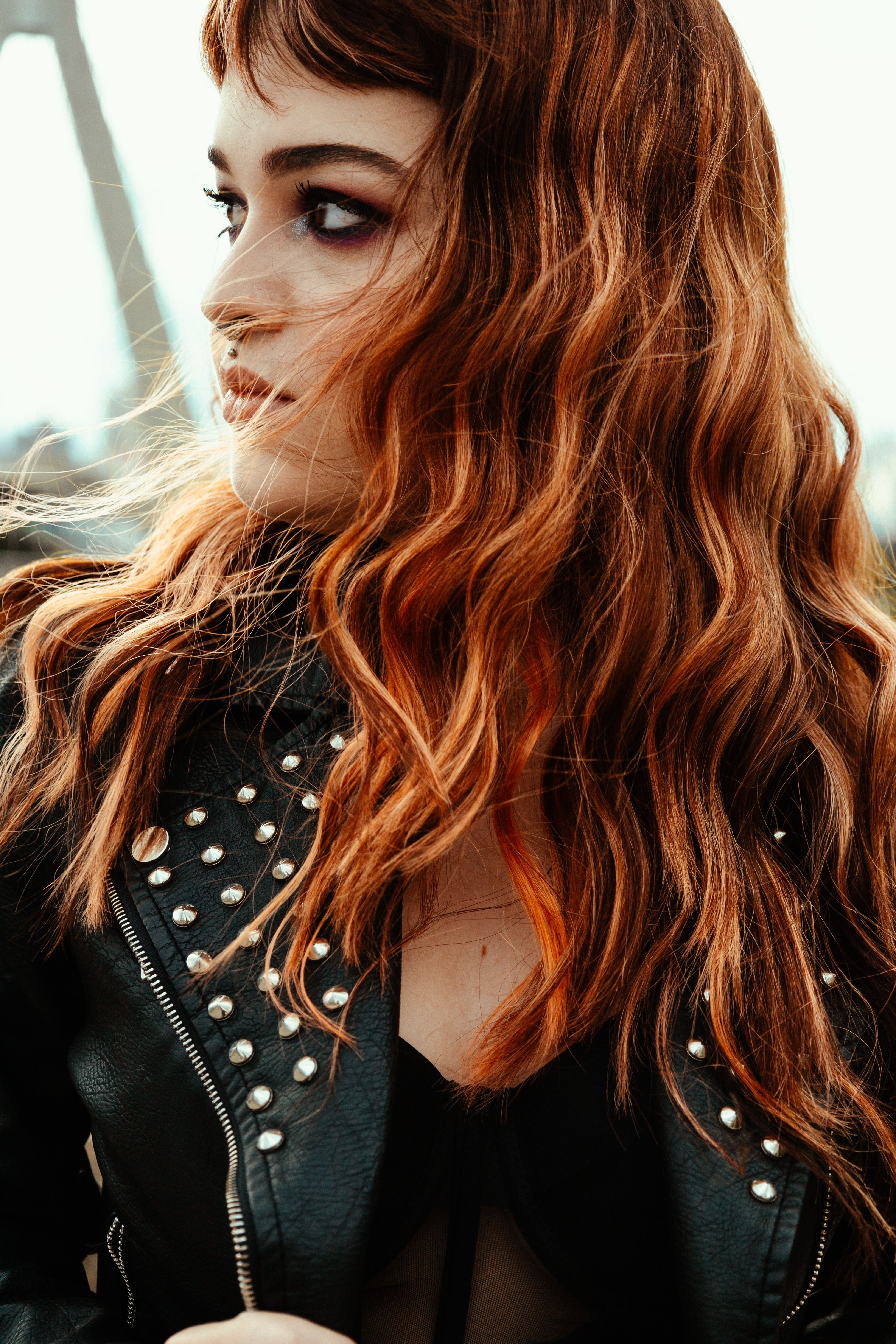 Stylish portrait of a woman with red hair in a studded leather jacket outdoors.