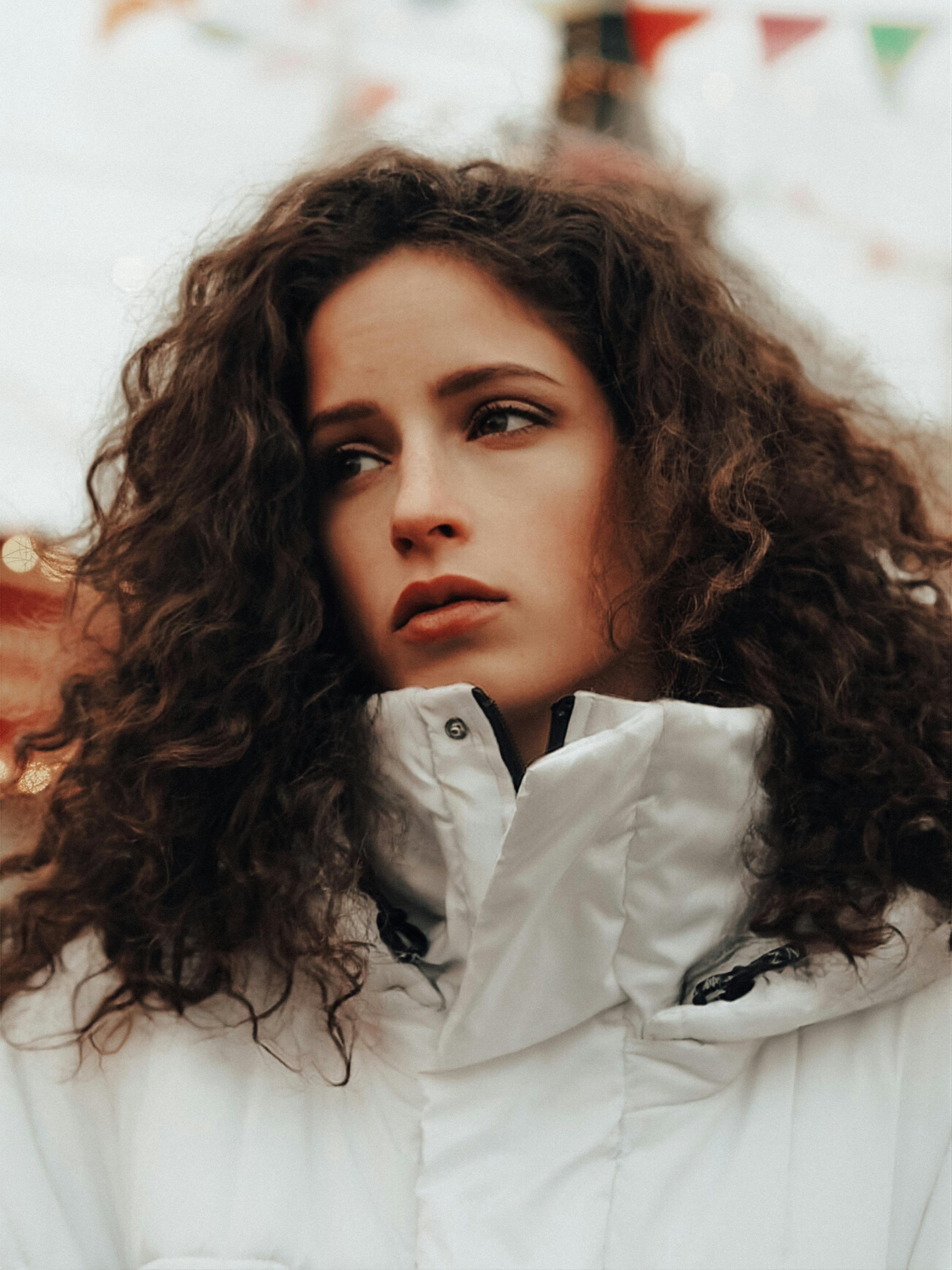 Close-up portrait of a woman with curly hair in a white jacket, set outdoors.