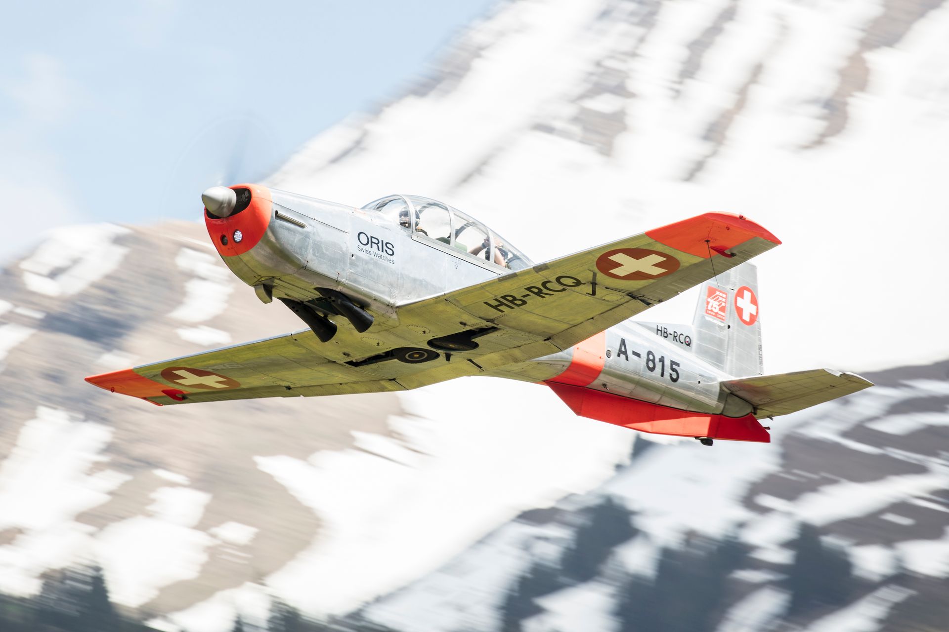 Vintage Swiss airplane flying over snowy mountains in daylight, showcasing aviation history and scenic travel.