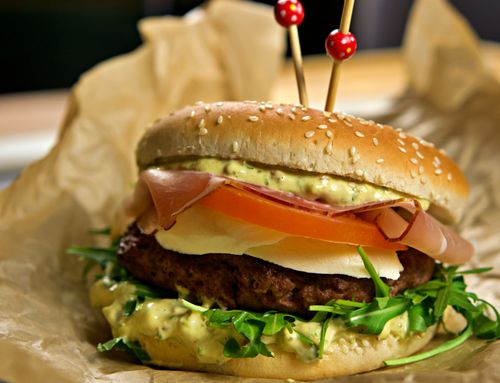 Free Delicious gourmet burger with cheese, ham, and tomato on a sesame bun, perfect for food photography. Stock Photo
