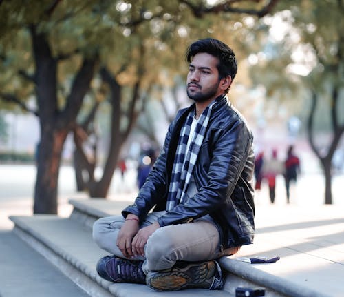 A Man in Black Leather Jacket Sitting on Concrete Steps