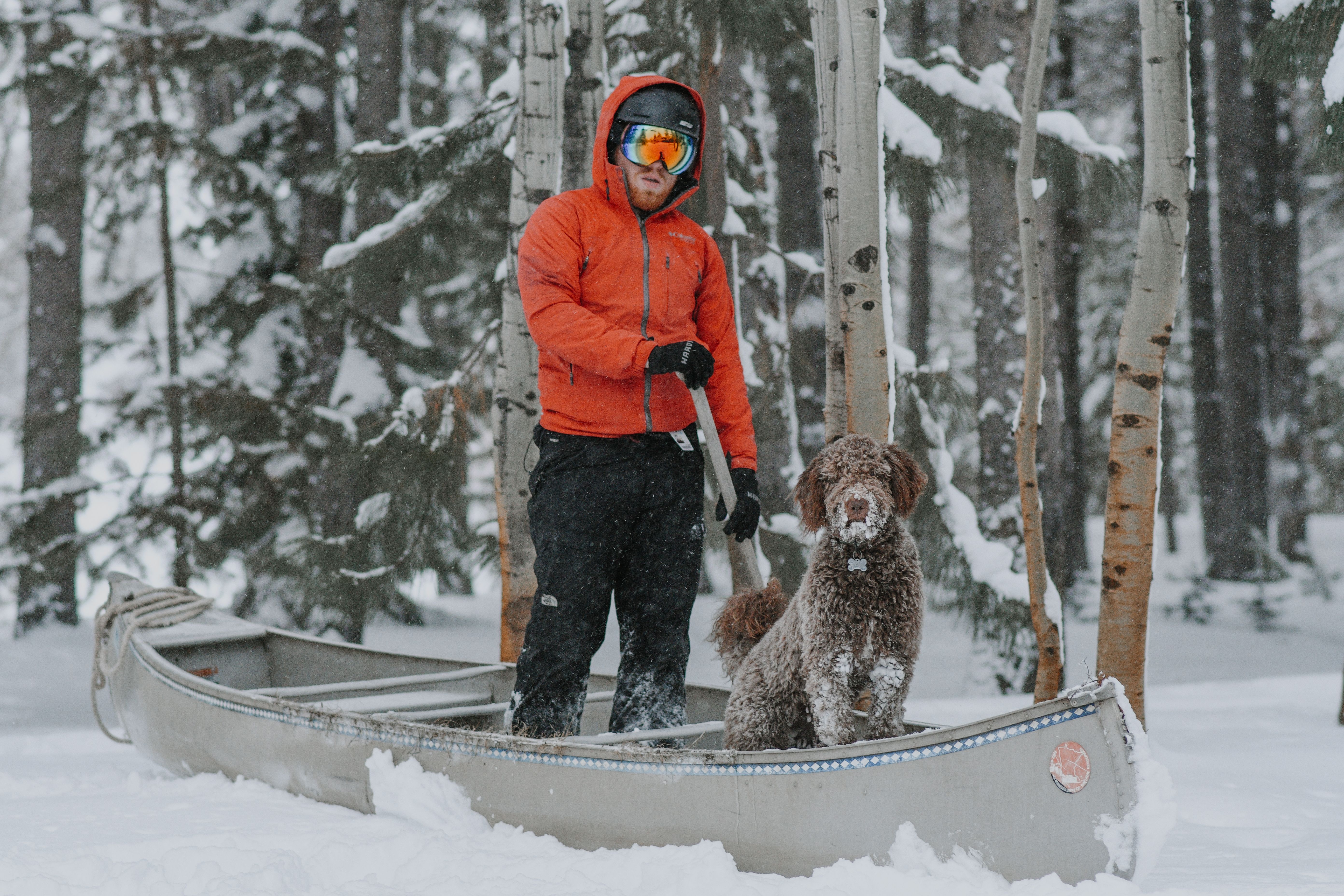 Free A man with his dog in a canoe amidst a snowy forest landscape, evoking winter adventure. Stock Photo