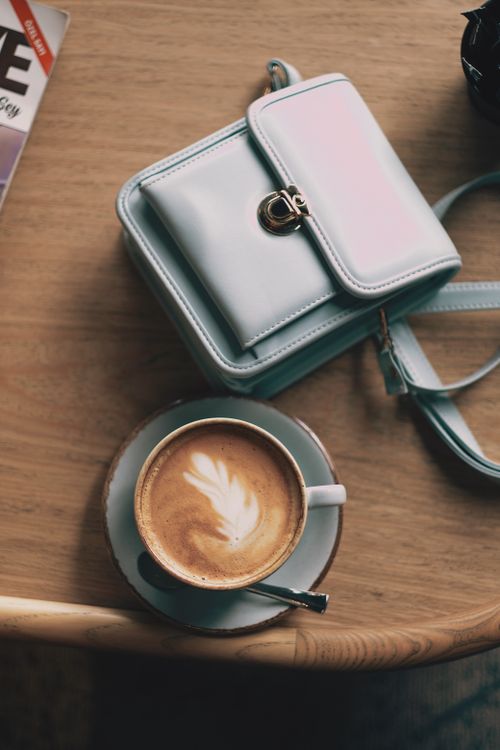 Free Top view of cappuccino with latte art beside a chic leather bag, ideal for lifestyle themes. Stock Photo