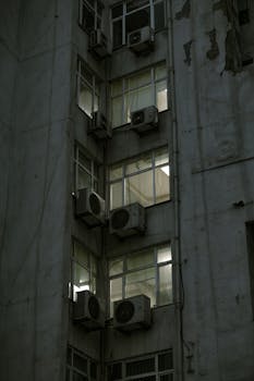 Low-angle view of an urban building facade with multiple air conditioners attached.