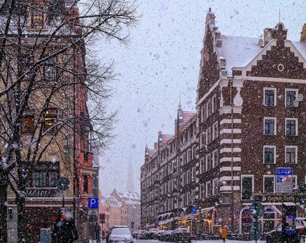 A picturesque snowfall captures a vibrant historical city street lined with charming buildings.